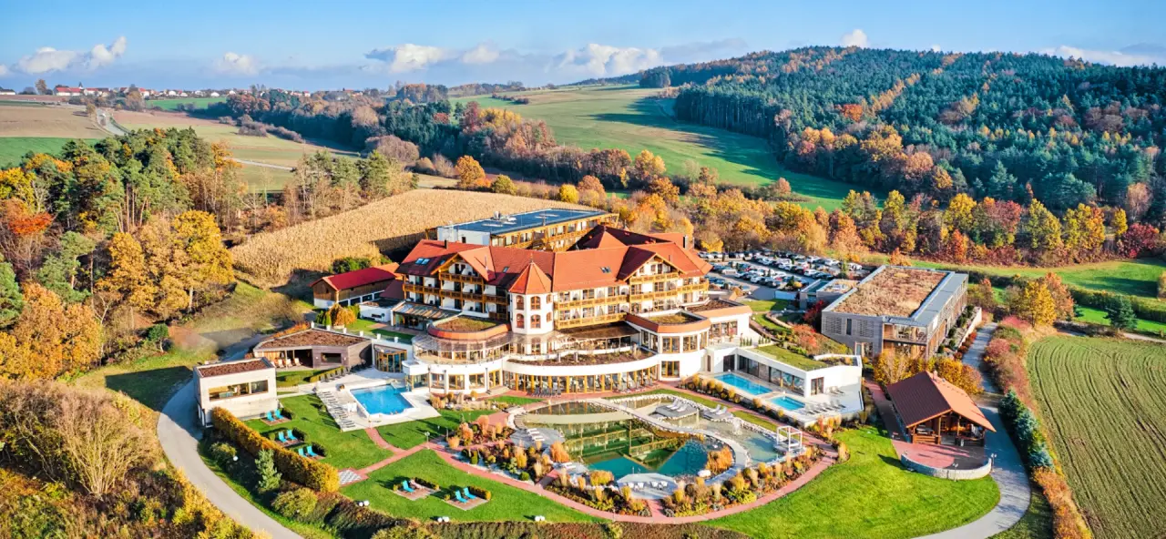 Luftaufnahme des Der Birkenhof Spa & Genuss Resort mit Hotelanlage, Pools und Naturteich, umgeben von herbstlicher Landschaft.