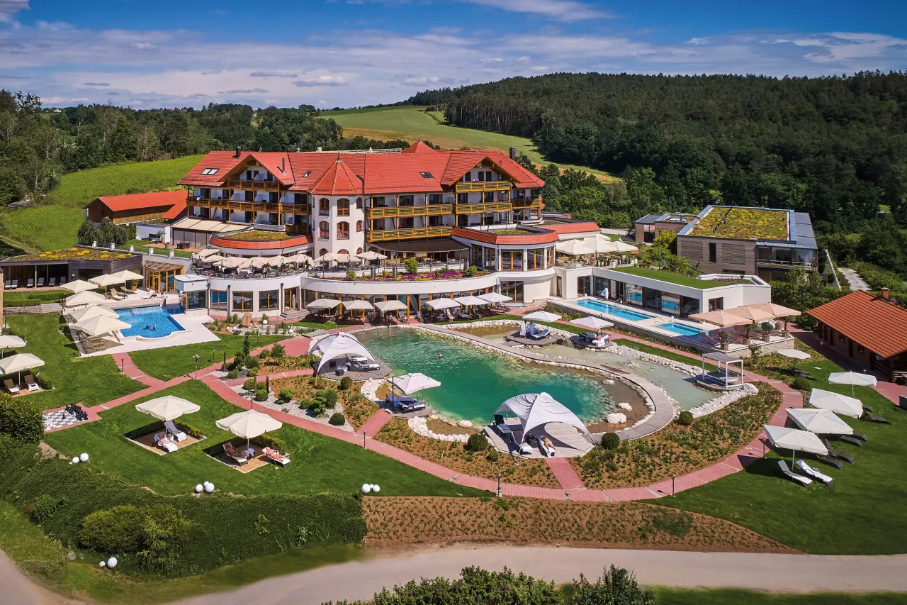 Luftaufnahme des Der Birkenhof Spa & Genuss Resort mit weitläufiger Poollandschaft, Naturbadeteich und grüner Umgebung.