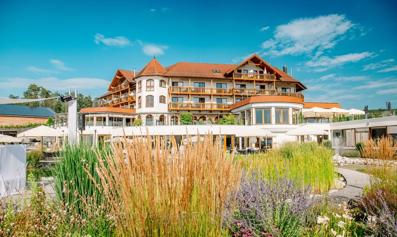 Aussenansicht des Der Birkenhof Spa & Genuss Resort mit blühendem Garten und blauem Himmel.