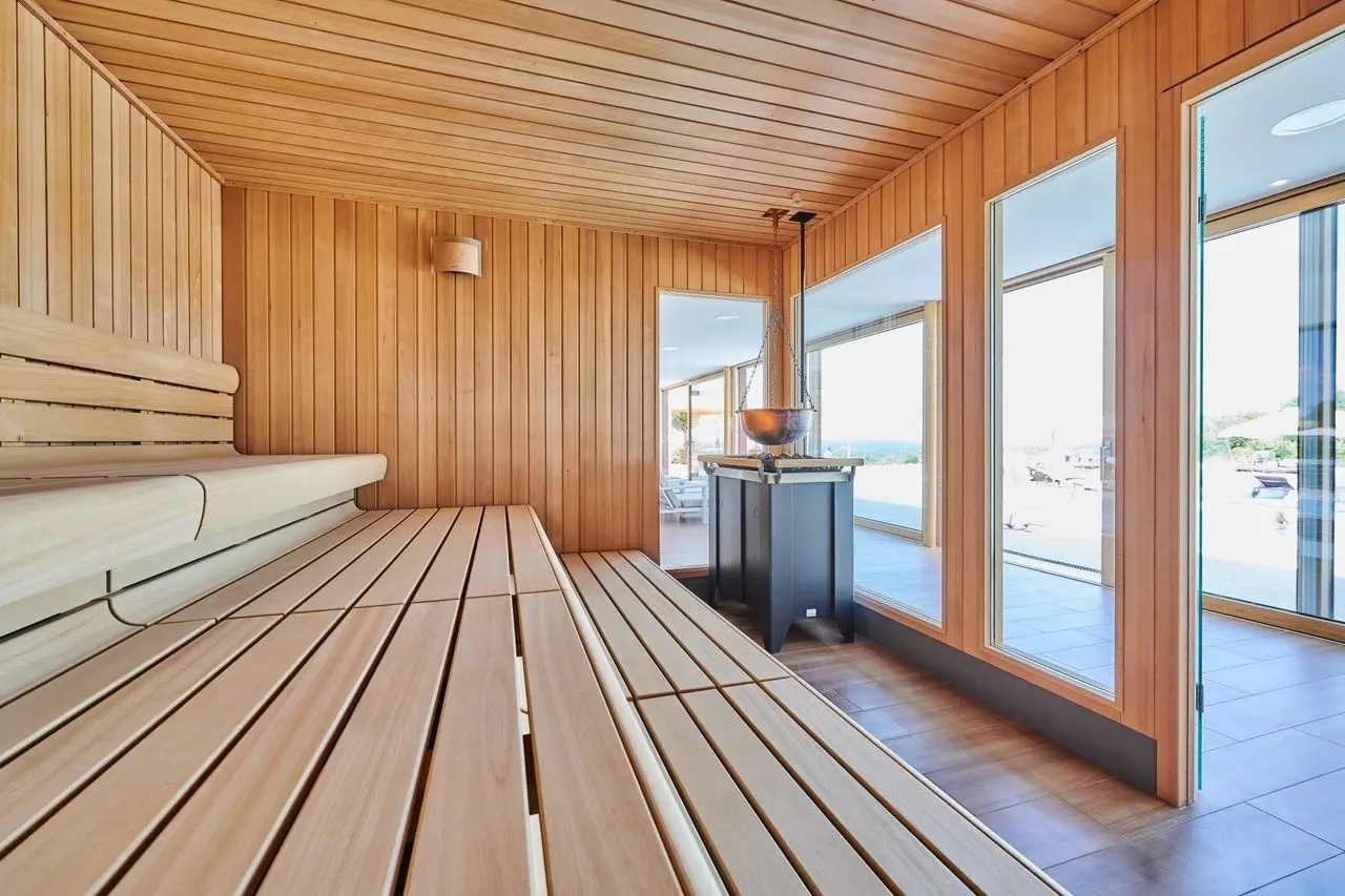 Moderne finnische Sauna mit großen Panoramafenstern und Blick ins Grüne im Der Birkenhof Spa & Genuss Resort.