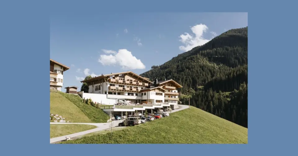 Panoramablick auf das Hotel Thurnerhof in den österreichischen Alpen, umgeben von grünen Wiesen und bewaldeten Bergen unter blauem Himmel.