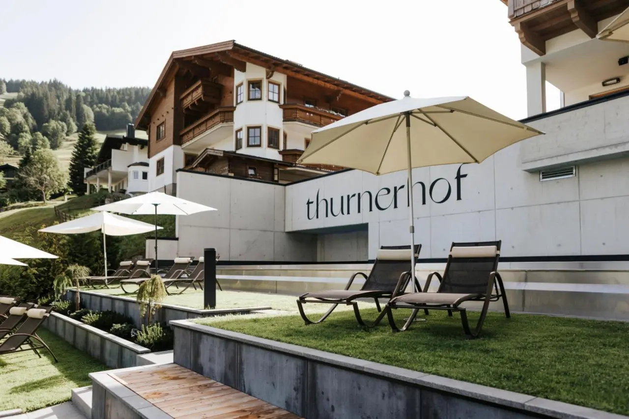 Aussenansicht des Thurnerhof Hotels mit alpiner Architektur, sonniger Liegewiese und Liegestühlen im Wellness-Garten.