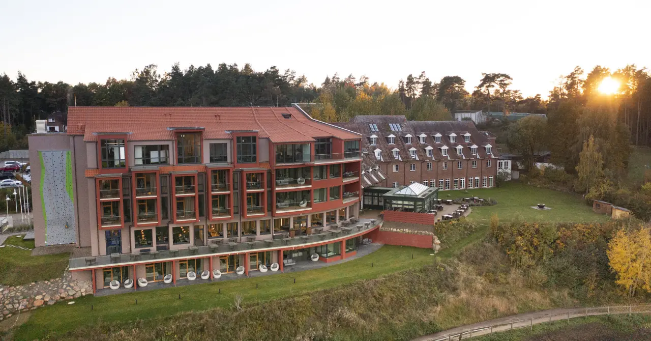 Panoramablick auf das Hotel Bornmühle im warmen Abendlicht, umgeben von Wald, mit moderner Architektur und Kletterwand.