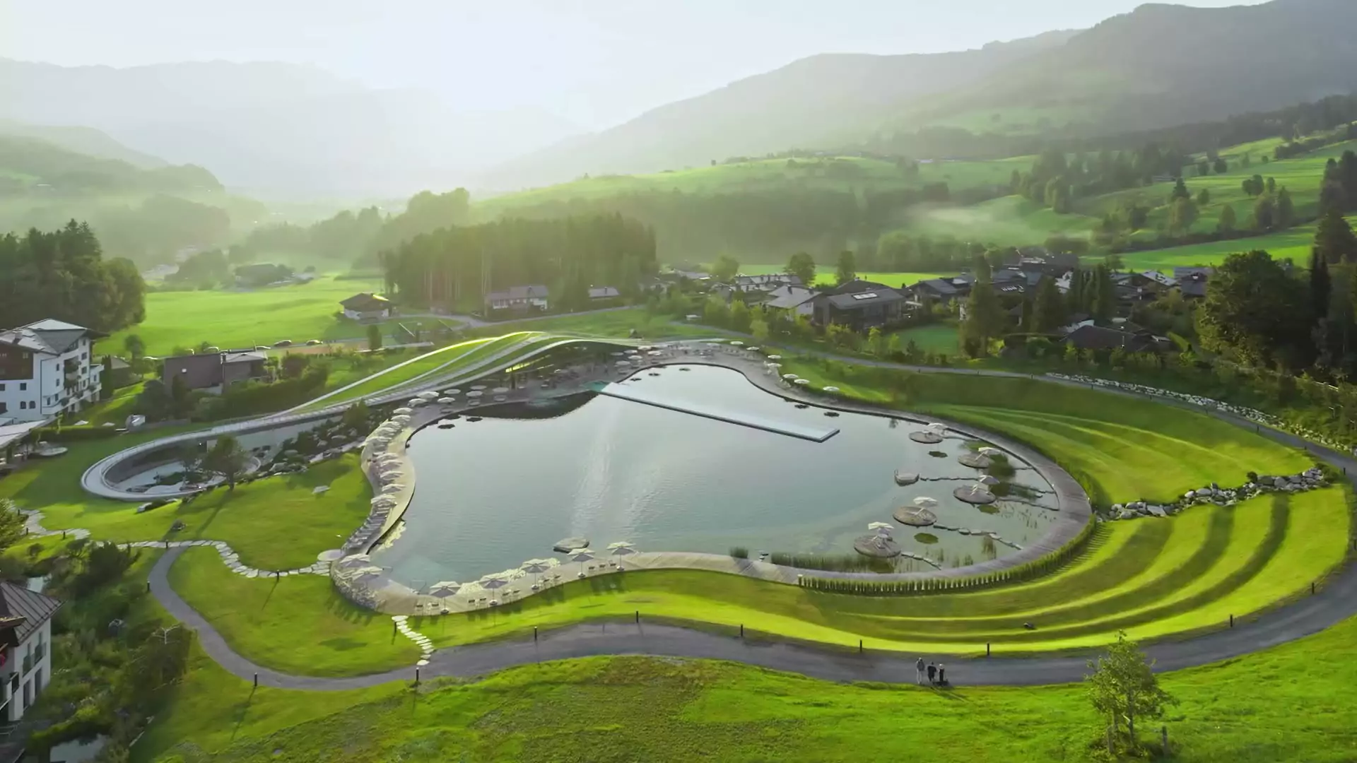Wellnesshotel Krallerhof in Leogang – Weitläufiger Naturbadeteich mit Hotelanlage und Bergen | Wellnesshotel Salzburger Land