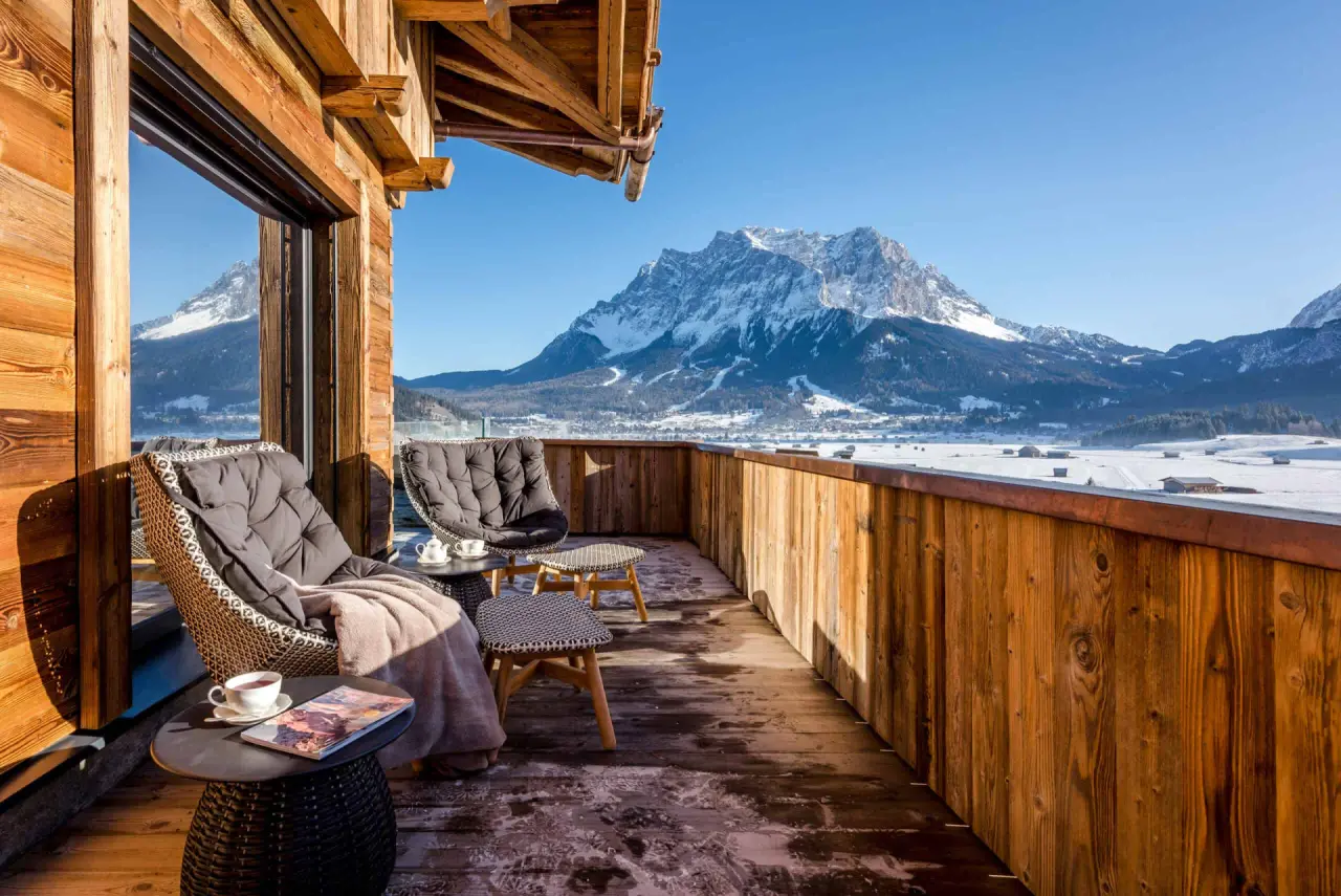 Balkon mit gemütlichen Sitzgelegenheiten und atemberaubendem Blick auf die verschneite Zugspitze im Hotel Post Lermoos.