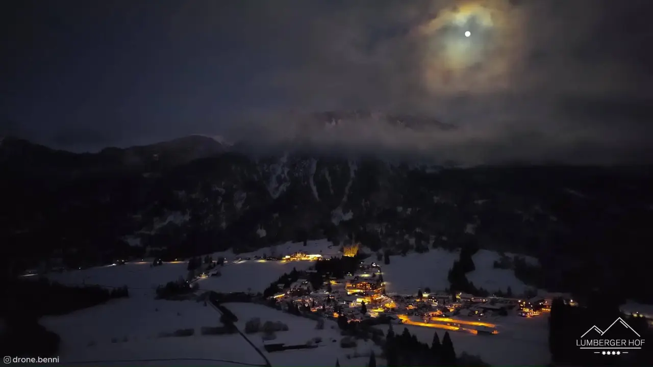 Nachtaufnahme des Hotel Lumberger Hof in verschneiter Berglandschaft mit beleuchtetem Dorf unter dem Mond.