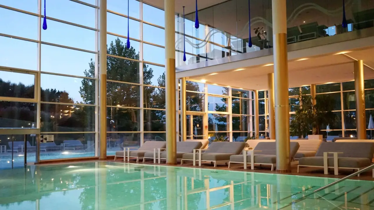 Geräumiger Innenpool mit großen Glasfronten und Liegebereich im SPA RESORT STYRIA bei Dämmerung.