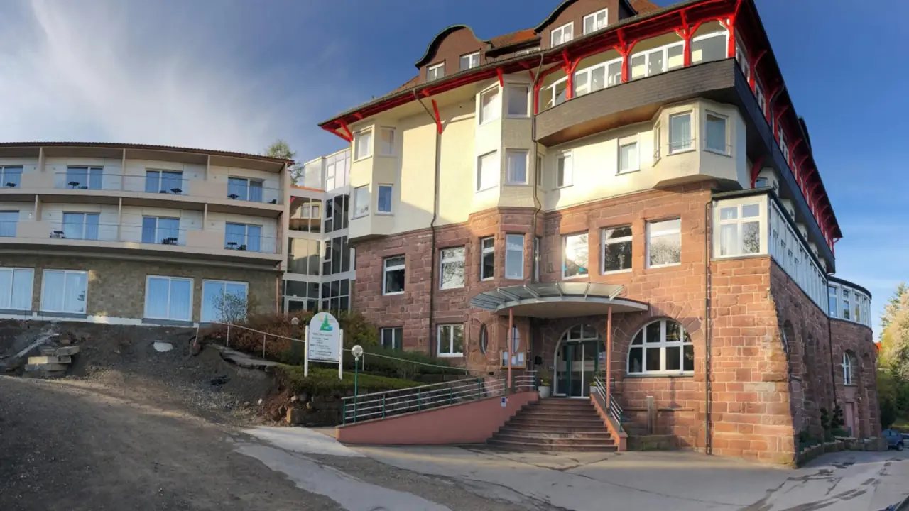Aussenansicht des Hotel Teuchelwald mit traditioneller Architektur und modernem Anbau unter blauem Himmel.