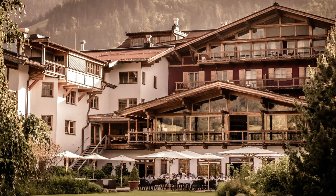 Traditionelle Aussenansicht des Hotel Kitzhof Mountain Design Resort mit Holzfassaden, Balkonen und sonniger Gartenterrasse.