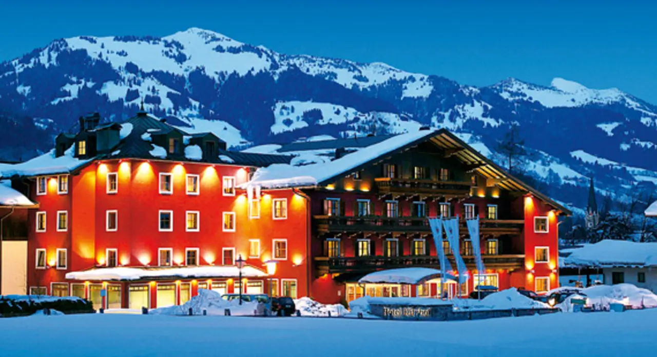 Hotel Kitzhof Mountain Design Resort in Kitzbühel bei Abenddämmerung, umgeben von verschneiten Alpen. Einladende Winteransicht.
