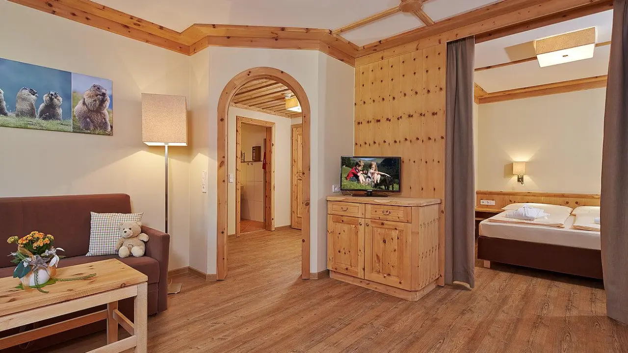 Geräumiges Familienzimmer im Hopfgarten Familotel Tirol mit Wohnbereich, Schlafzimmer und rustikalen Holzmöbeln.