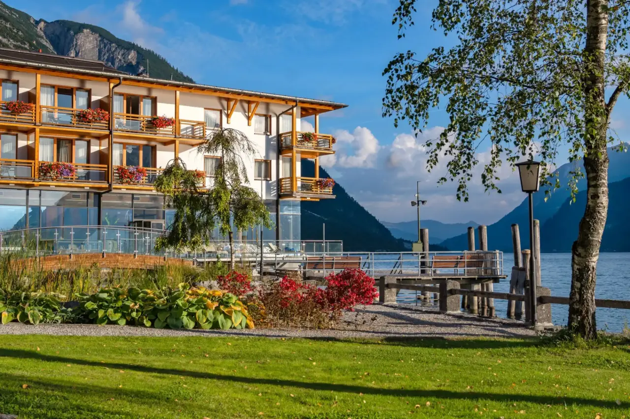 Travel Charme Fürstenhaus Am Achensee: Hotelgebäude mit blumengeschmückten Balkonen direkt am Achensee und Bergpanorama.