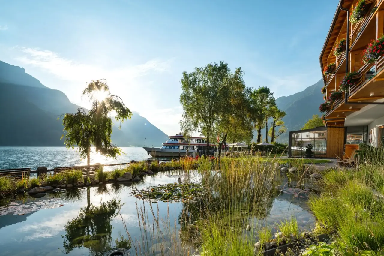 Travel Charme Fürstenhaus Am Achensee bei Sonnenlicht, direkt am See mit Naturteich und Bergpanorama.