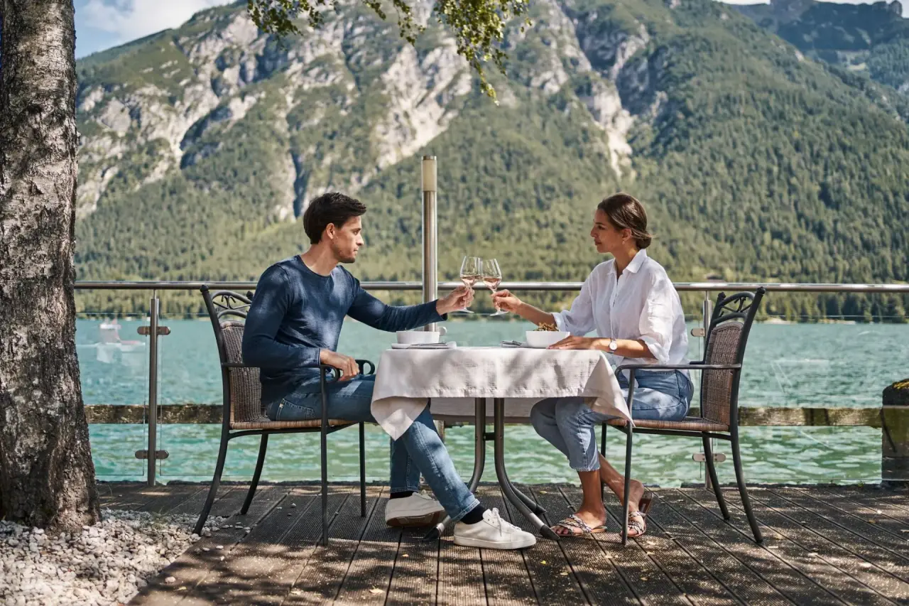 Paar beim Anstoßen auf der Seeterrasse des Travel Charme Fürstenhaus Am Achensee mit Bergblick.