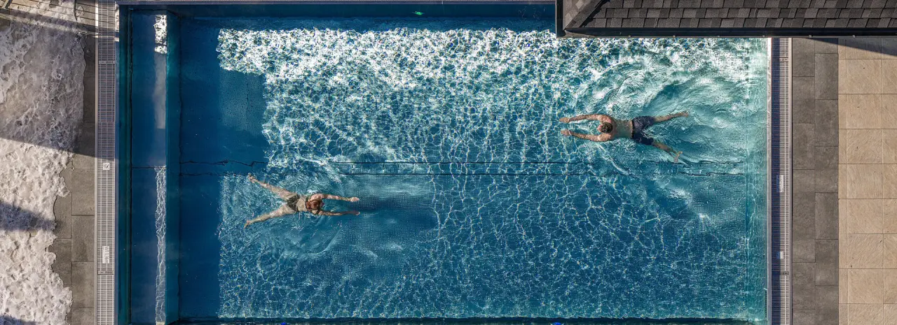 Draufsicht auf den Aussenpool des Hotel Post Kaltenbach mit zwei schwimmenden Gaesten und Wasserspielen.