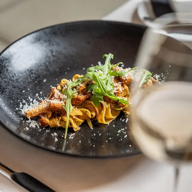 Frische Tagliatelle mit Pilzen, Rucola und Parmesan im Restaurant des Hotel Post Kaltenbach, serviert mit Weisswein.