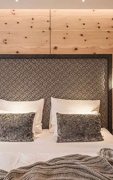 Gemütliches Doppelbett mit gepolstertem Kopfteil und Holzwand im Zimmer des Hotel Post Kaltenbach.
