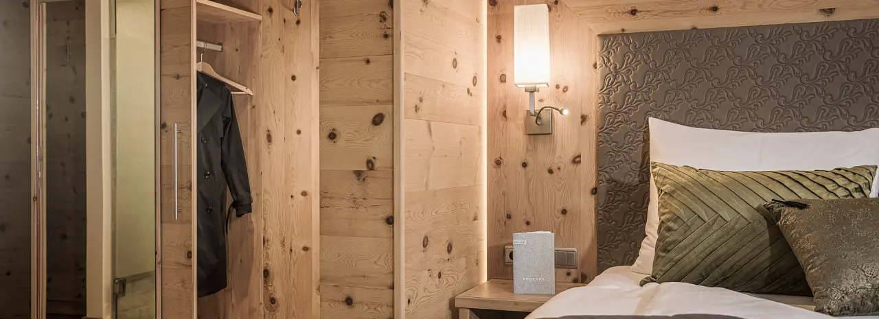 Detailansicht eines gemütlichen Hotelzimmers mit Holzwänden, Bett und Leselampe im Hotel Post Kaltenbach.