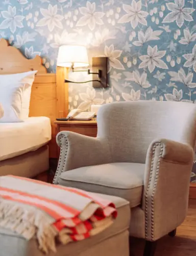 Gemütlicher Sessel mit Leselampe und floraler Tapete im komfortablen Hotelzimmer des Landhaus am Stein.