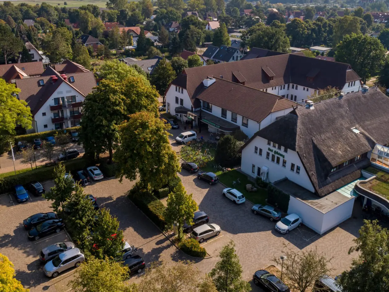 Luftaufnahme des Hotel Warnemünder Hof mit mehreren Gebäuden, Parkplätzen und viel Grün in einer ruhigen Umgebung.