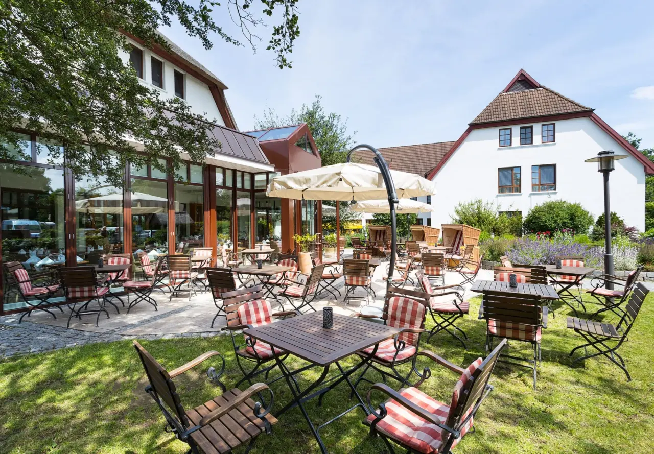 Einladende Gartenterrasse mit Holztischen, gestreiften Stühlen und Strandkörben im Hotel Warnemünder Hof.