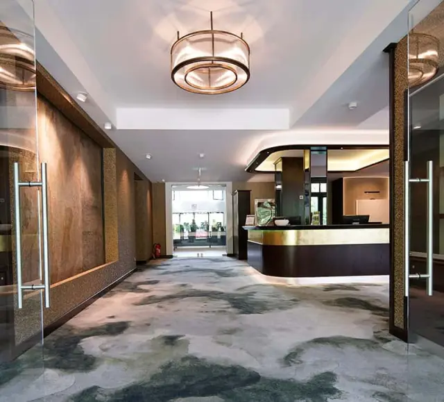Moderne Hotellobby des Essensio Hotels mit Rezeption, stilvollem Teppich und indirekter Beleuchtung.