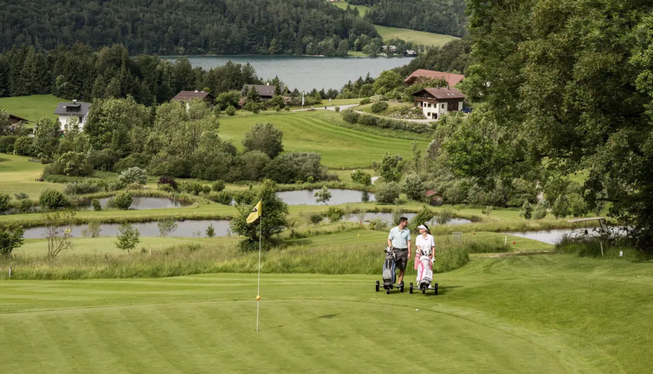 Paar beim Golfen auf dem hoteleigenen Golfplatz mit See- und Waldpanorama im Hotel Ebner's Waldhof am See.