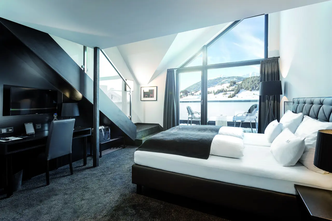 Modernes Hotelzimmer im Das Marent mit Doppelbett, Schreibtisch und Balkon mit atemberaubendem Bergblick im Winter.