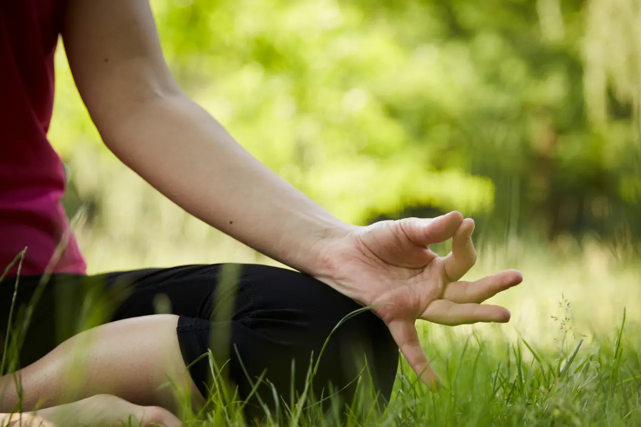 Nahaufnahme einer meditierenden Person im Gras des relexa hotel Bad Steben, symbolisiert Ruhe und Wellness.