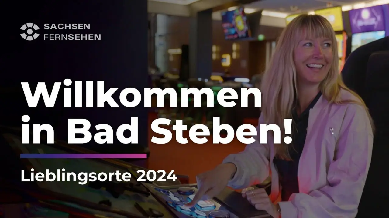 Lachende Frau bedient interaktiven Bildschirm in einem Unterhaltungsbereich im relexa hotel Bad Steben, mit 'Sachsen Fernsehen' Logo.