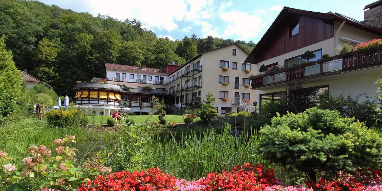 Aussenansicht des Gesundheits- und VitalCenter Gollée mit üppigem Garten, Teich und Waldumgebung.