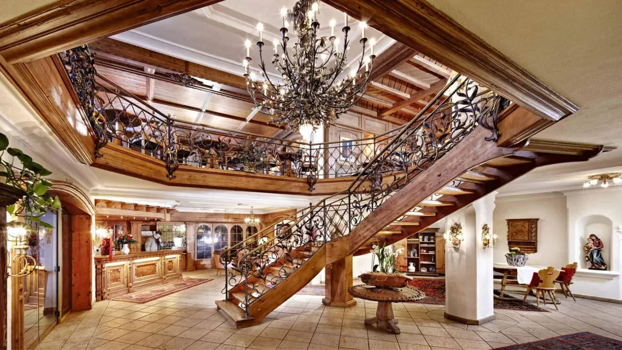 Prächtige Lobby mit Holztreppe, schmiedeeisernem Geländer und Kronleuchter im Relais & Chateaux Hotel Singer.