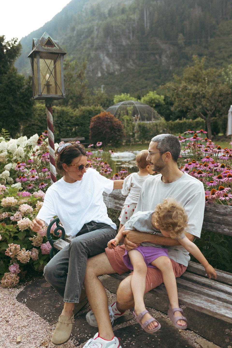 Neuhaus Zillertal Resort in Mayrhofen – Familie entspannt auf einer Bank im blühenden Hotelgarten | Wellnesshotel Zillertal