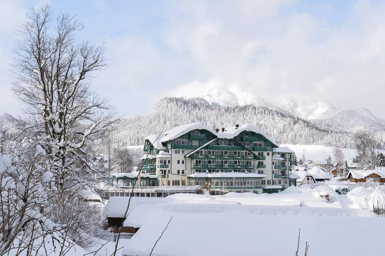 Romantik Hotel Seevilla im Winter mit schneebedeckten Bergen und Bäumen. Idyllische Aussenansicht des Wellnesshotels.