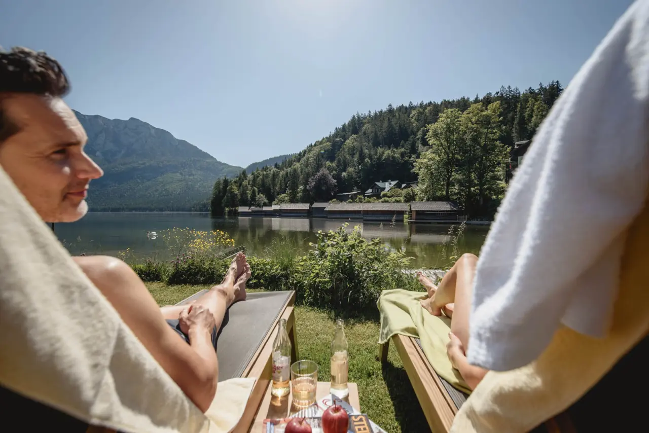 Gäste entspannen auf Sonnenliegen am Grundlsee mit Bergpanorama und Bootshäusern im Romantik Hotel Seevilla.
