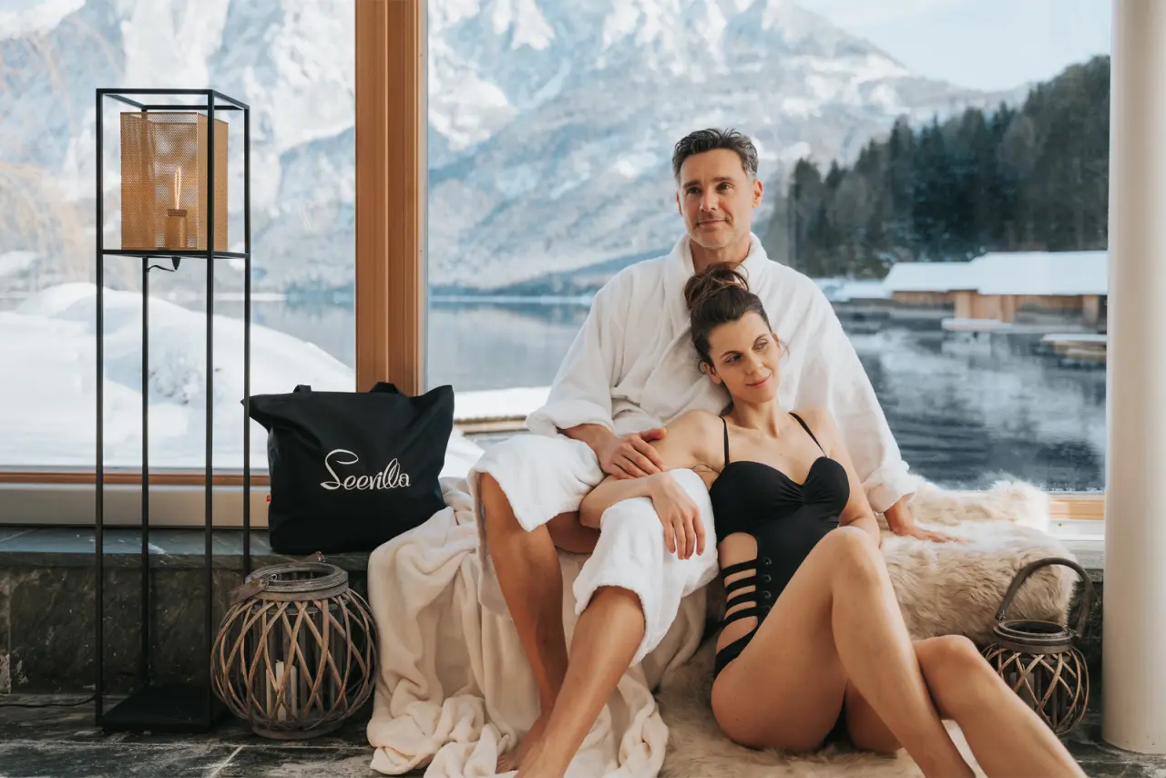 Entspanntes Paar im Bademantel mit Seeblick und Bergpanorama im Wellnessbereich des Romantik Hotel Seevilla.