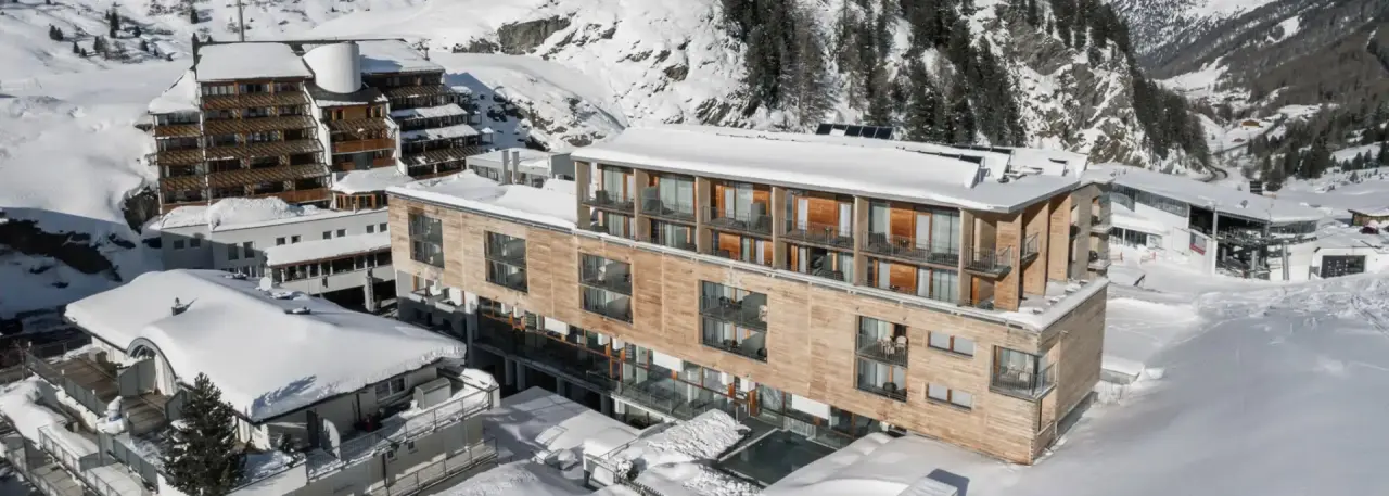 Modernes Hotel The Crystal VAYA Unique in verschneiter Alpenlandschaft. Winteransicht mit Balkonen und Bergpanorama.