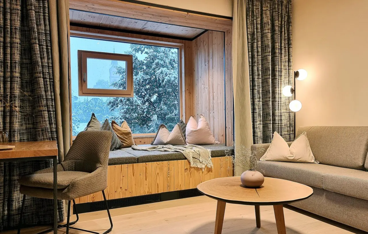 Gemütliche Suite im Hotel Matschner mit Leseecke, Sofa und Blick auf verschneite Landschaft.