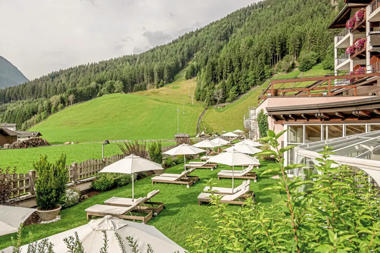 Garten mit Liegestühlen und Sonnenschirmen vor bewaldetem Berghang im Wellness & Relax Hotel Milderer Hof.