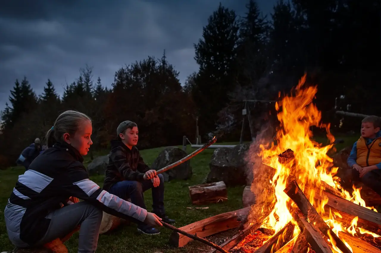 Gemütliches Lagerfeuer mit Kindern im Aussenbereich des Sporthotel Grafenwald am Abend.
