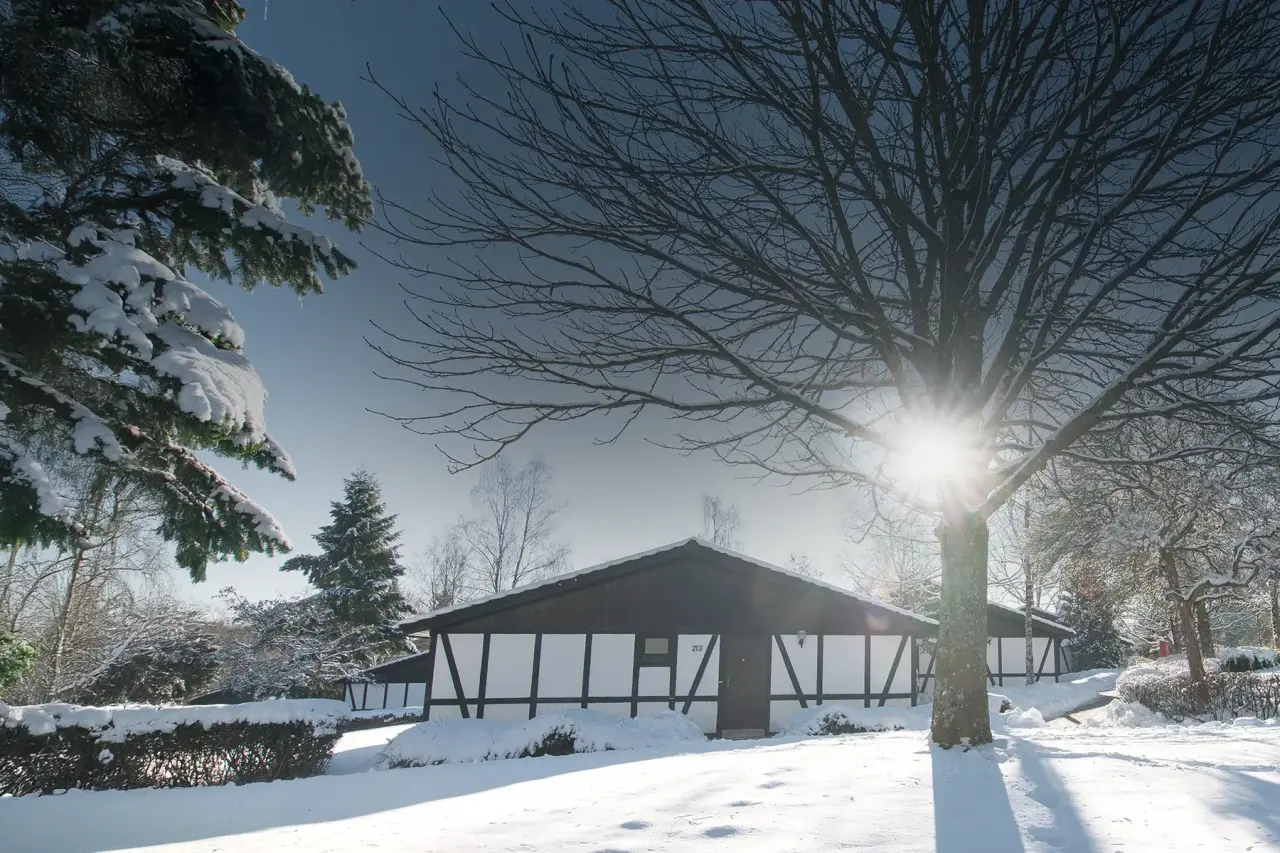 Sporthotel Grafenwald im Winter: Ein schneebedecktes Fachwerkhaus mit strahlender Wintersonne im Wald.