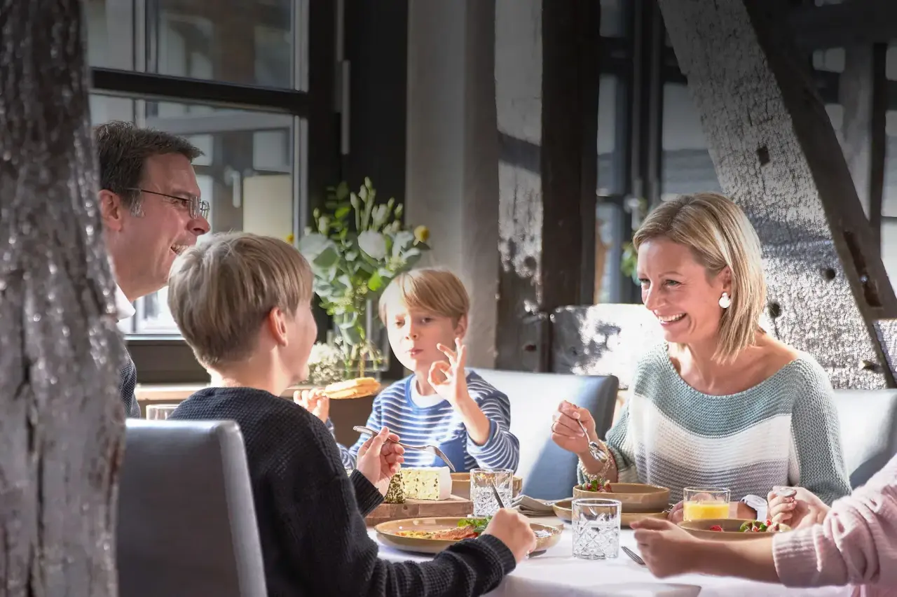 Glückliche Familie genießt ein Abendessen im Restaurant des Sporthotels Grafenwald. Helle, einladende Atmosphäre.