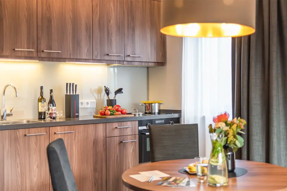 Moderne Küchenzeile mit Esstisch, frischen Lebensmitteln und Wein in einem Apartment des Sporthotels Grafenwald.