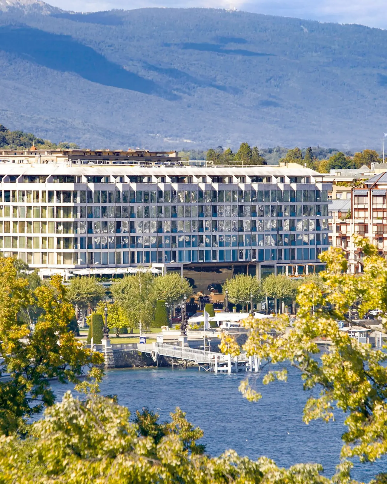 Fairmont Grand Hotel Geneva am Genfersee mit Alpenpanorama und grüner Uferpromenade.