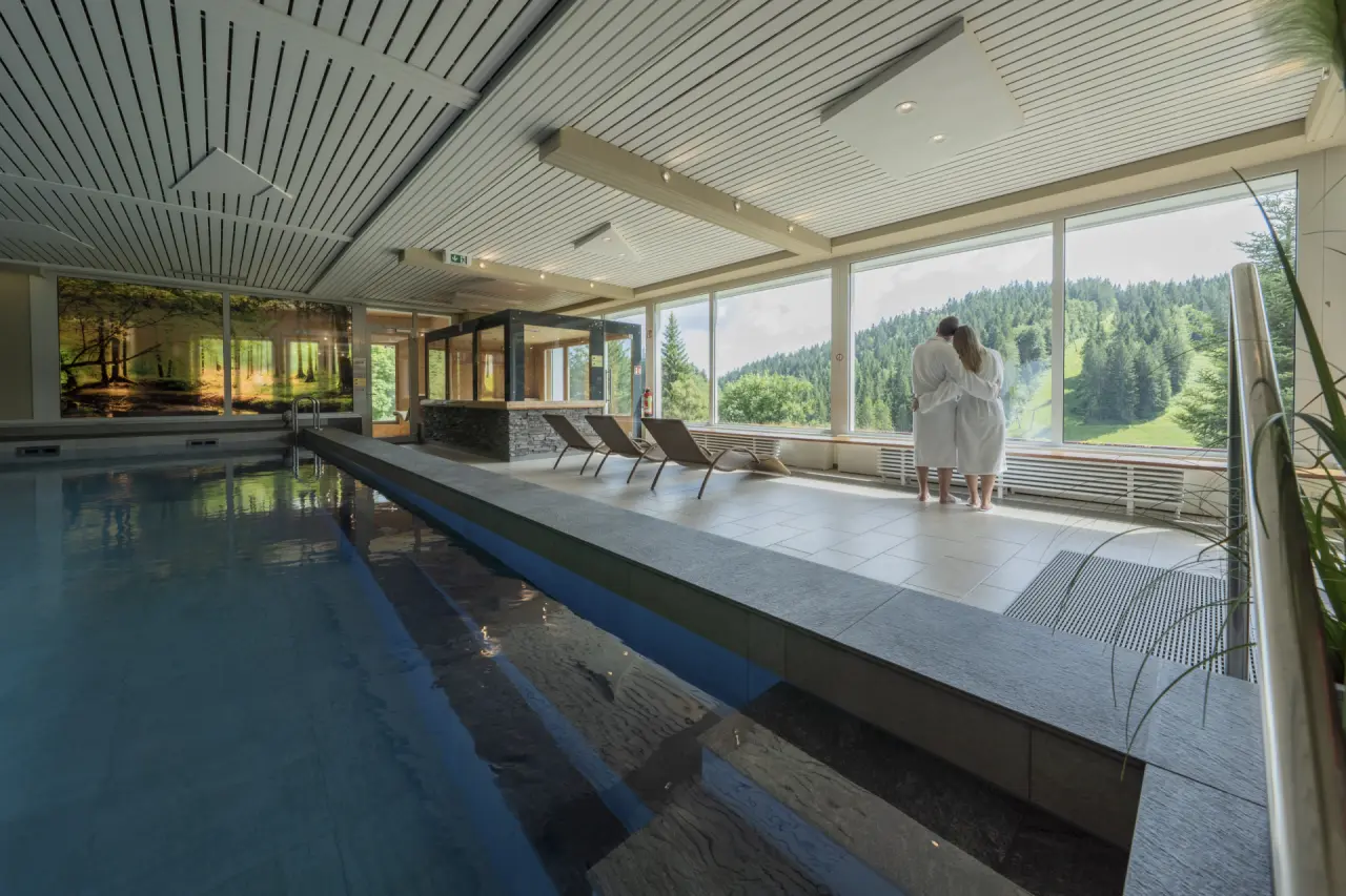 Innenpool mit Panoramablick auf den Schwarzwald und entspannendes Paar im Waldhotel am Notschreipass.