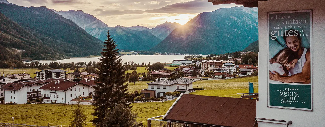 Malerischer Sonnenuntergang über dem Achensee und den Alpen, umgeben von einem Dorf. Panoramablick vom Hotel St. Georg zum See.