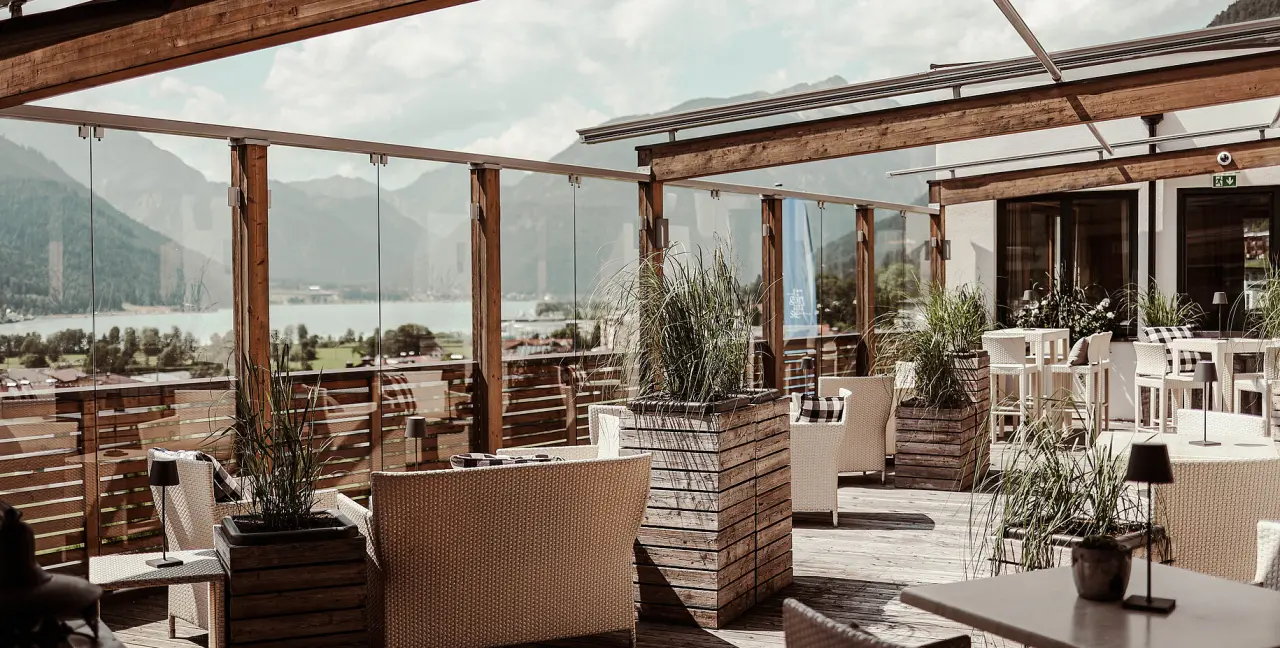 Einladende Hotelterrasse mit Rattanmöbeln, Pflanzen und Panoramablick auf den See und die Berge im Hotel St. Georg zum See.