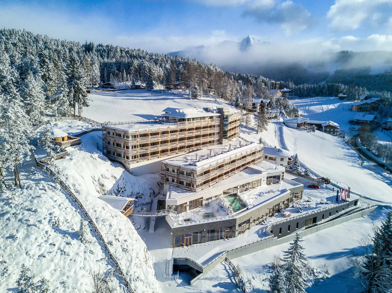 Winterliche Luftaufnahme des Hotel Nidum mit verschneiter Berglandschaft und beheiztem Aussenpool.