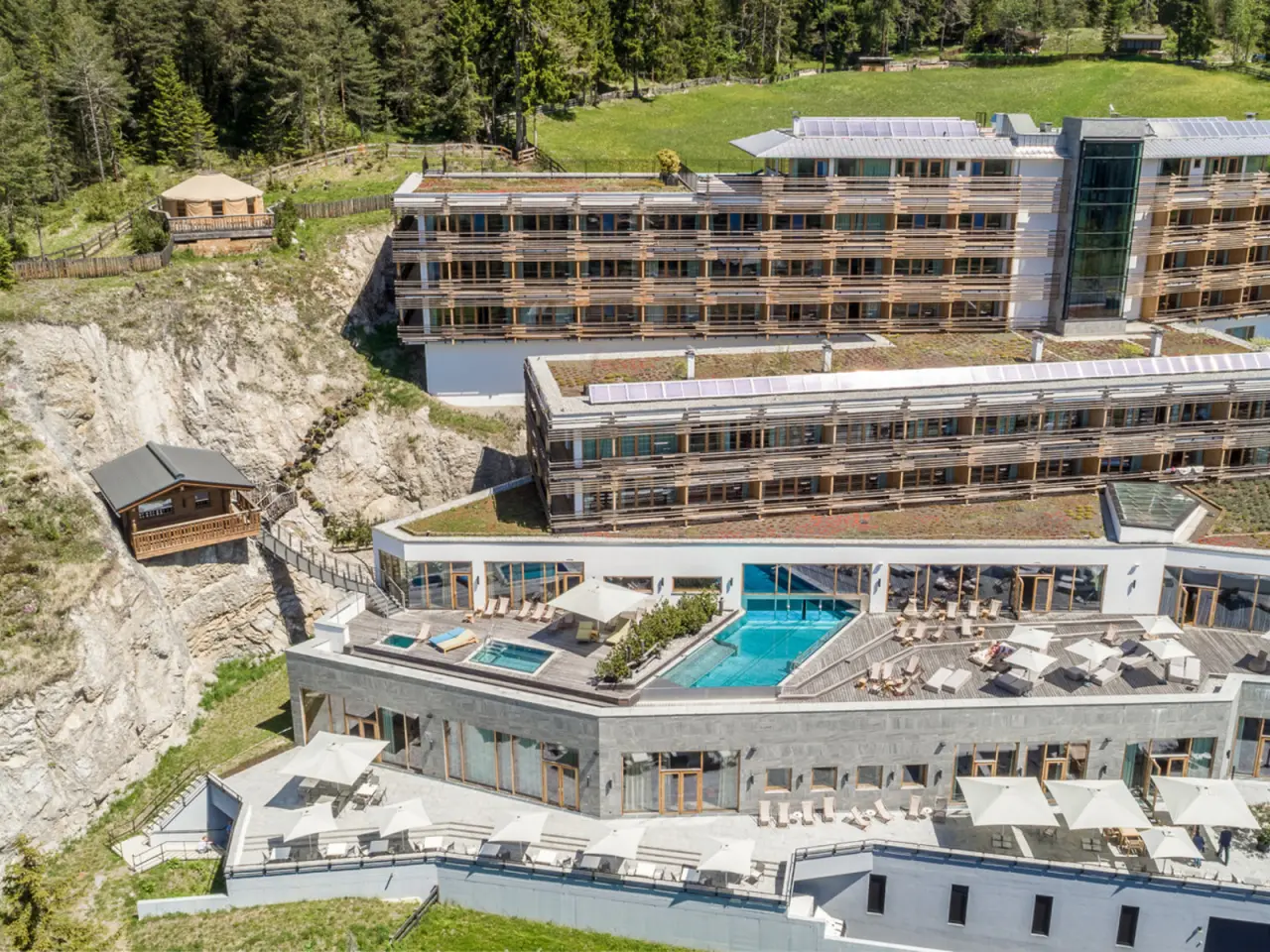 Luftbild des Hotel Nidum mit Infinity Pool, Sonnenterrassen und alpiner Waldlandschaft.