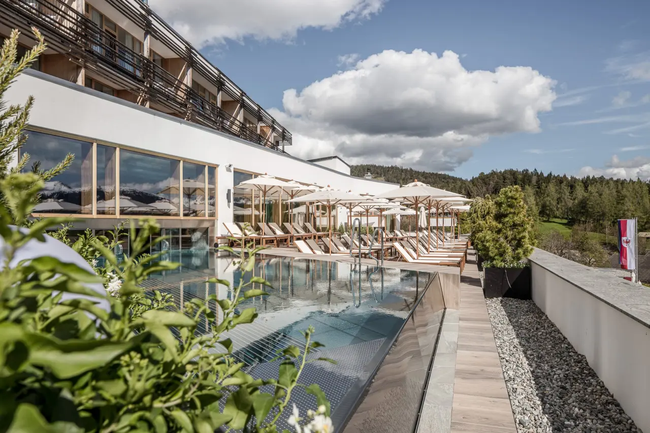 Aussenpool mit Sonnenliegen und Schirmen auf der Terrasse des Hotel Nidum, umgeben von Wald und Bergen unter blauem Himmel.
